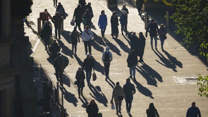 Pedestrians walk through the city centre in Leeds, casting long shadows on the ground