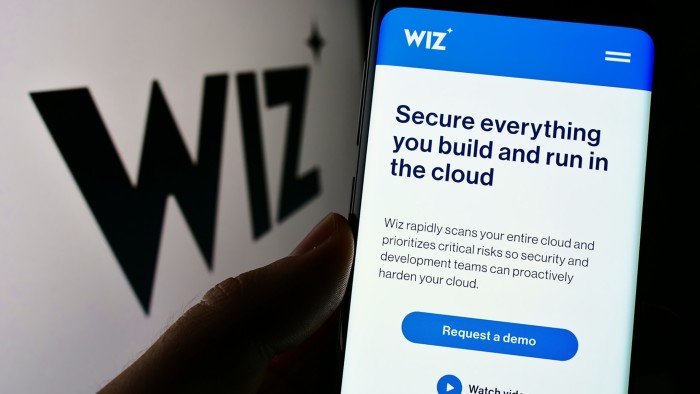 Person holding cellphone with webpage of US cloud security company Wiz Inc on screen in front of logo