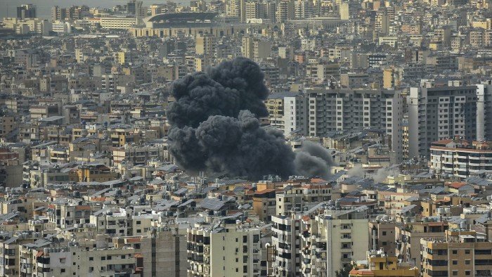 Thick black smoke rises from a densely populated area. The cityscape is filled with closely packed buildings
