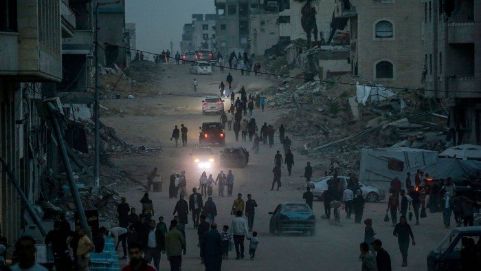 Palestinians walk along a dusty street lined with debris and destroyed buildings in Gaza City