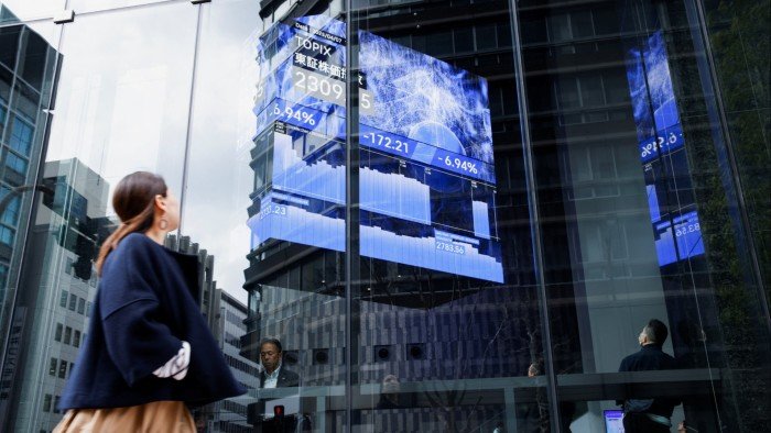 A woman walks past a stock quotation board at a brokerage in Tokyo, Japan