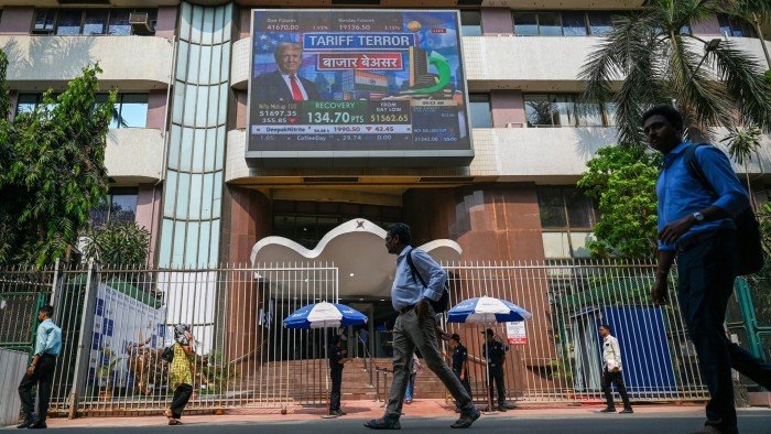 edestrians walk past a broadcast screen of the Bombay Stock Exchange